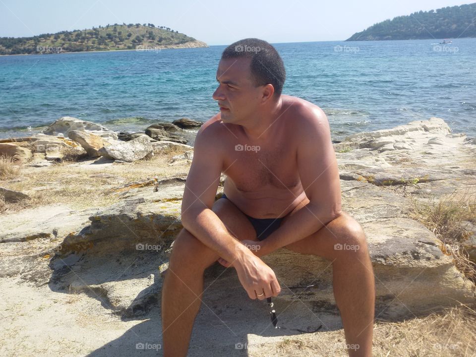 Man on beach, seating on rock