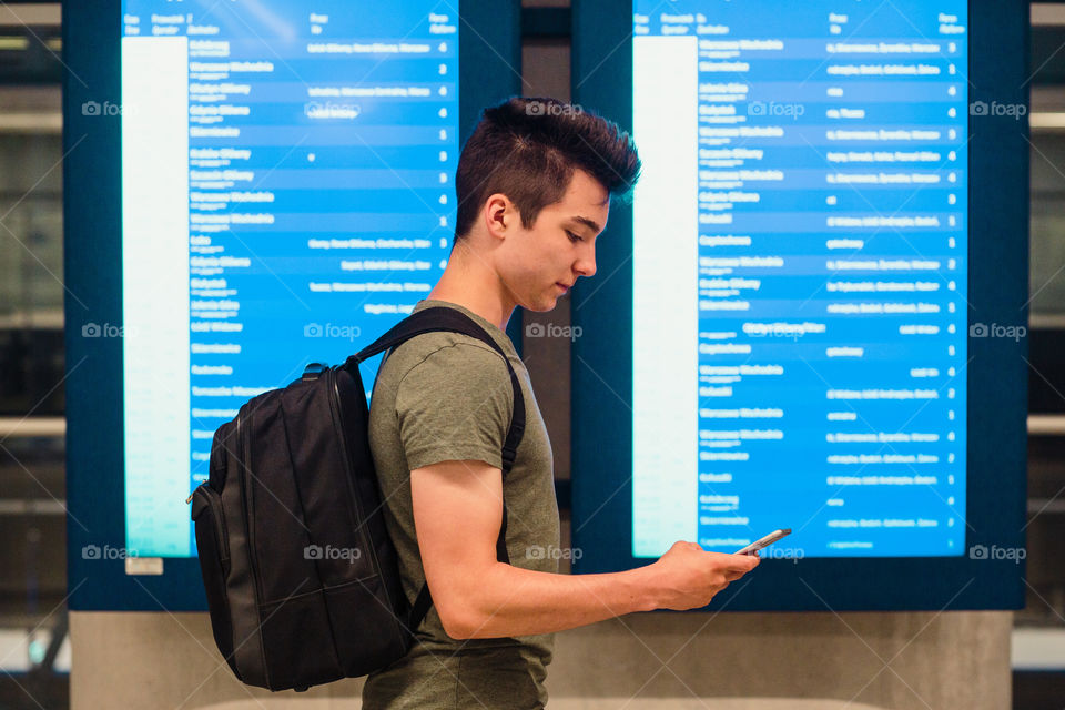 Young man standing in the railway station next to screens with schedule, planning a travel, travelling with backpack