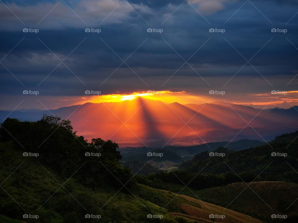 A sunburst sunset appears through the clouds at the top of Doi Samer Dao in Nan, Thailand.