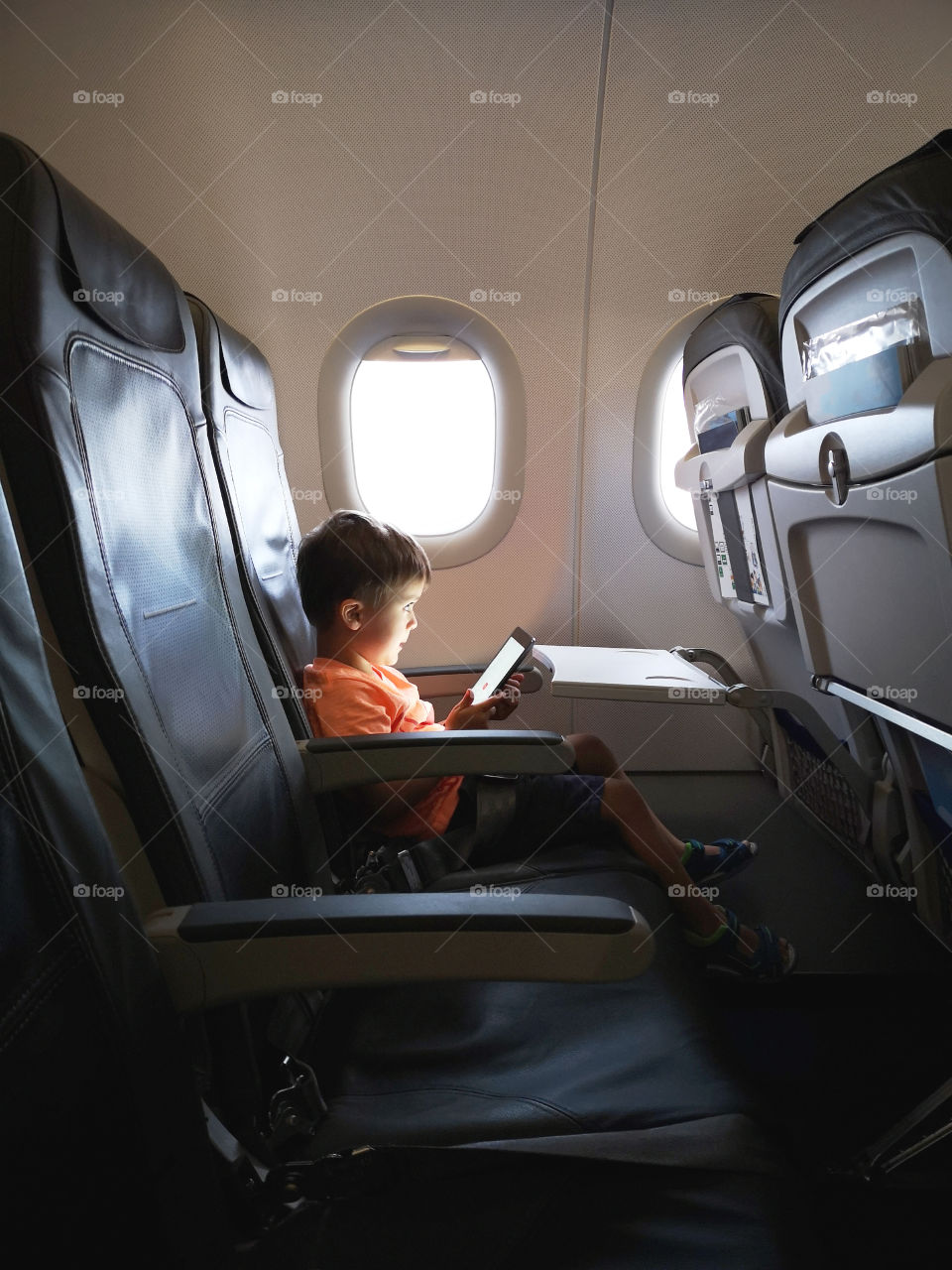 Little boy with digital tablet on board airplane.