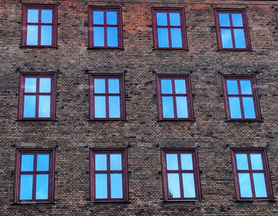 View to the old brick wall with symmetrical rectangular shape windows with bright blue sky reflection 