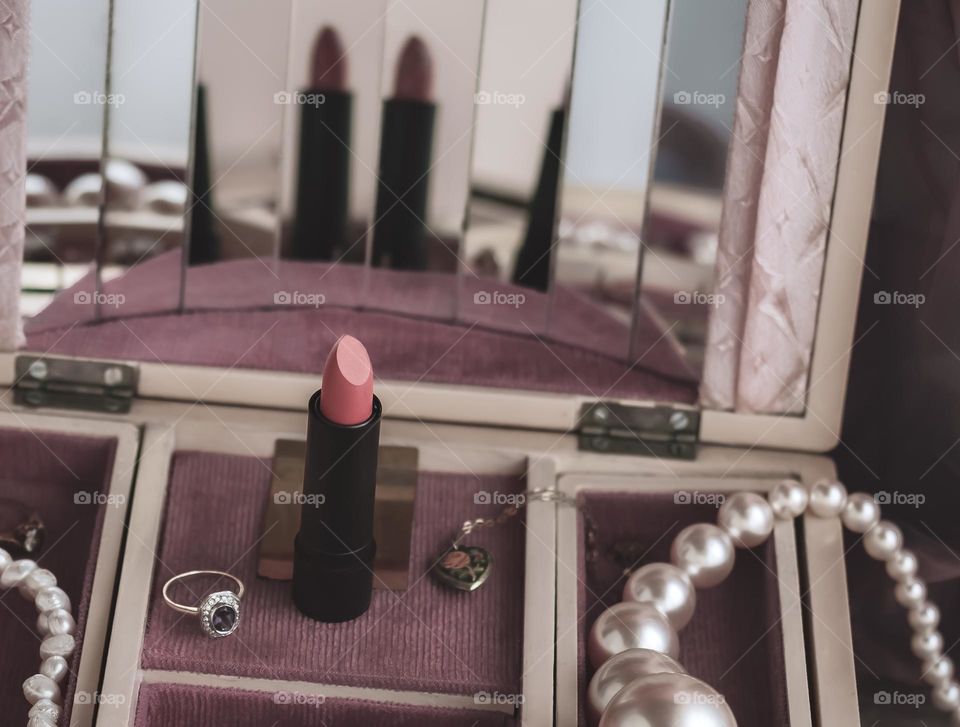 Vintage feel jewellery box with pearls and rings, with a warm pinky lipstick as the focus and reflected in the mirrors behind