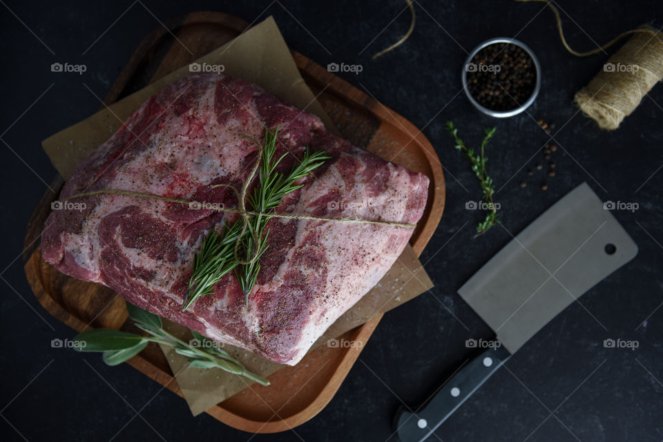 Natural light on a flat lay of a pork shoulder prepped for cooking with fresh herbs and a meat cleaver