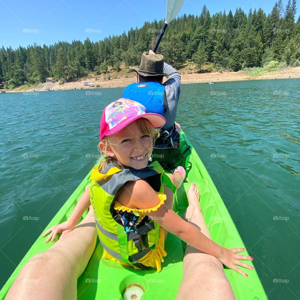 Little girl kayaking on beautiful blue lake with her family 