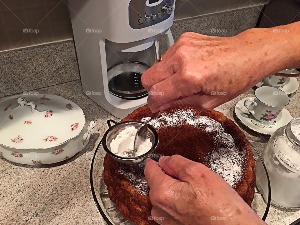 Homemade cake being topped with powdered sugar by skilled hands.