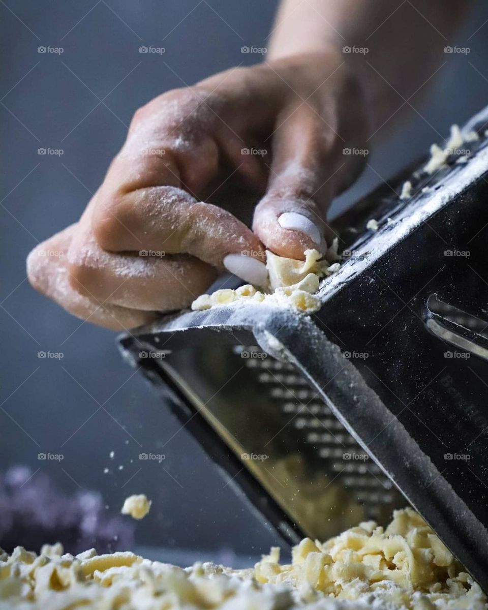 The chef's uniform in the kitchen is tearing the dough for the future pie on a grater on the table flour and flowers