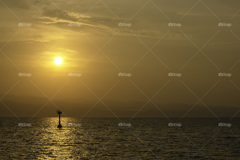 Golden light of sunrise behind the mountains and the shadow of signal lamp for sailing in the sea.