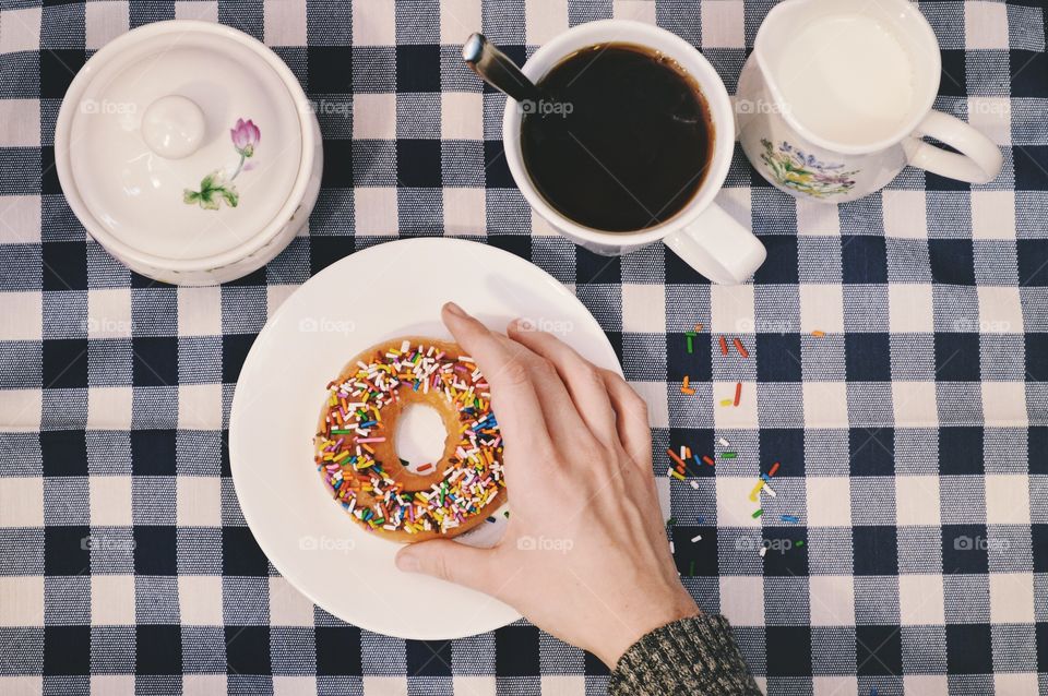 Person's hand with donut and cup of coffee
