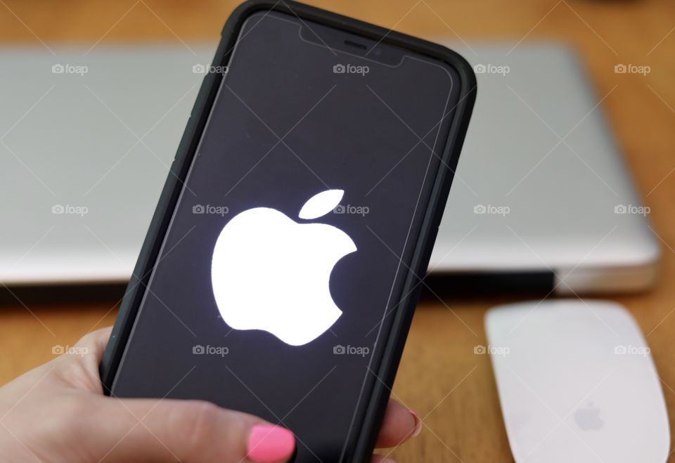 Holding Iphone 11 pro Max with Logo and Apple products in background