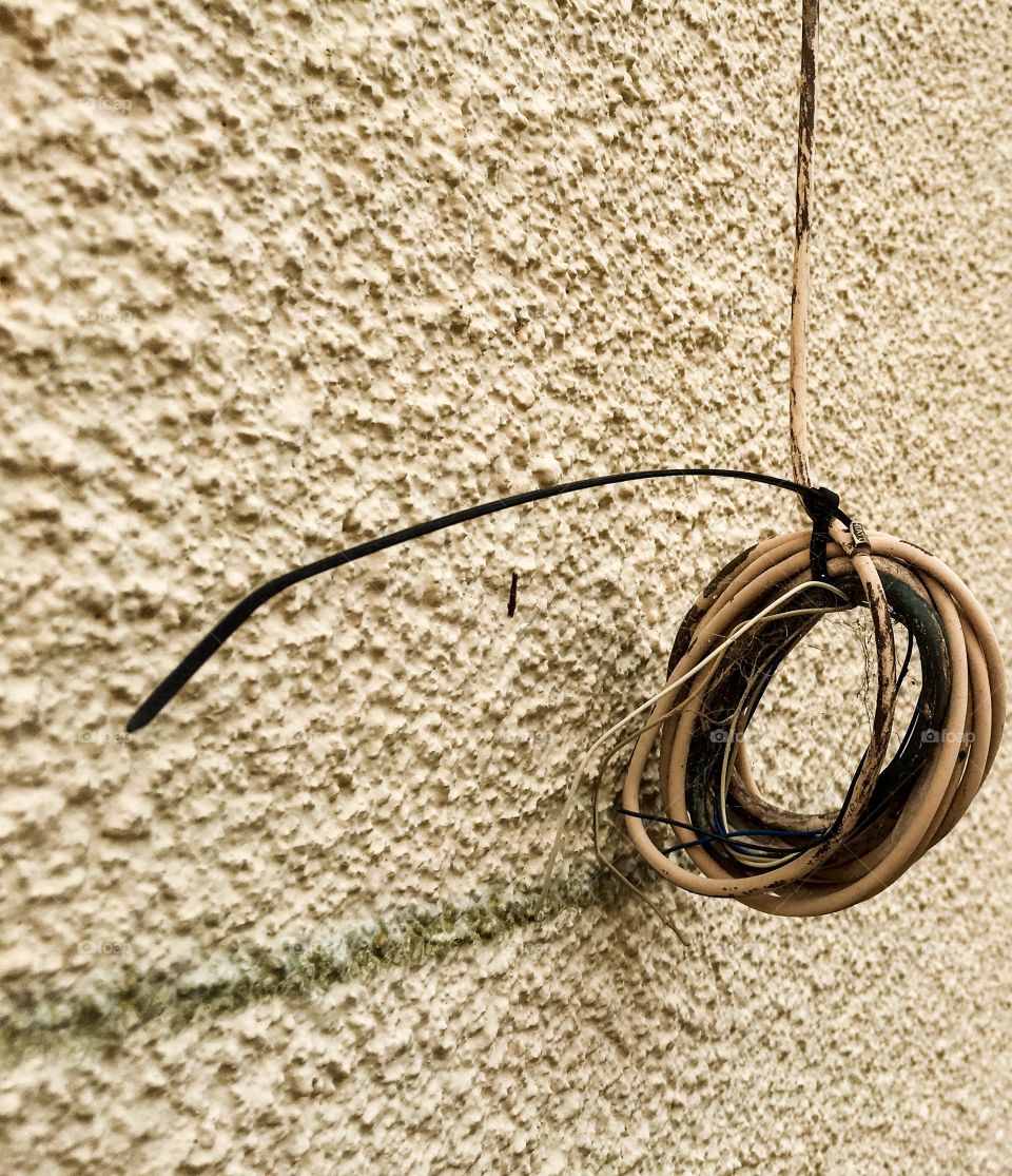 Old house wire cooked up hanging from roof, against old stucco wall grunge art background