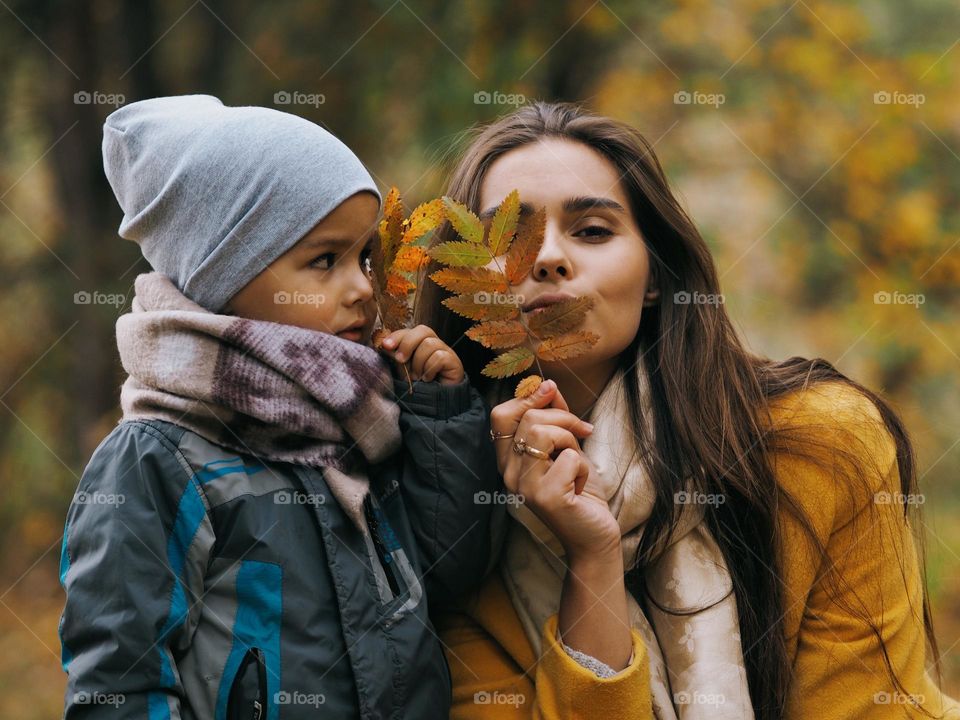 Young beautiful mom with little son in the autumn forest