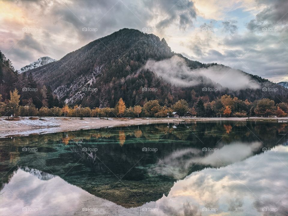 Scenic view of the beautiful reflection of foggy mountains in the green lake in Alps, Slovenia.