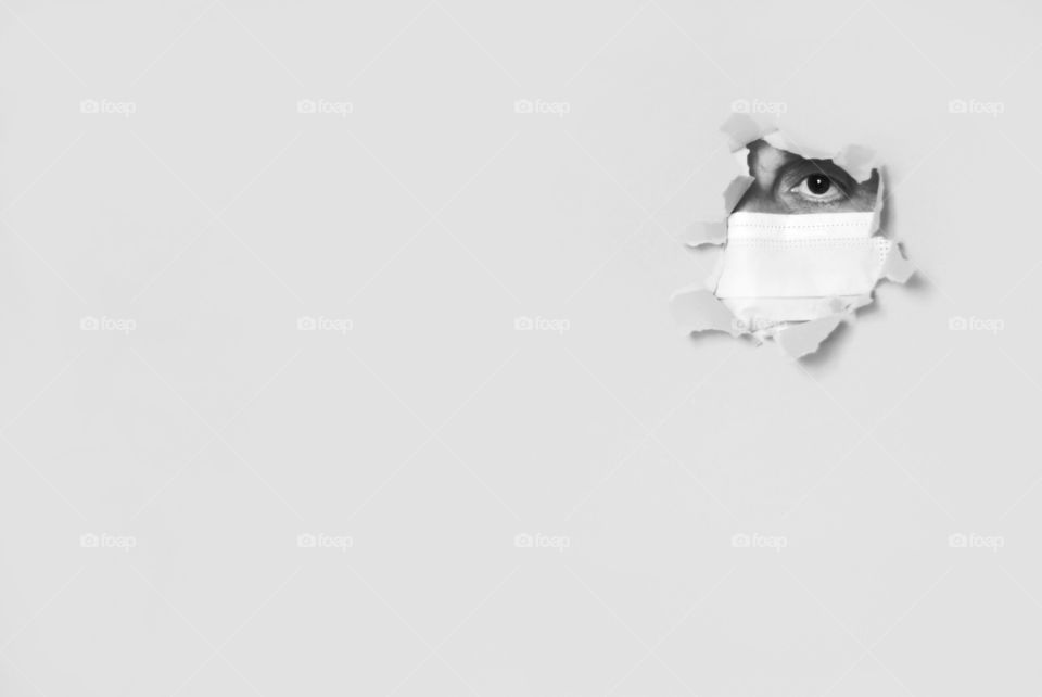 Woman's face with protective face mask behind a hole in paper background, black and white