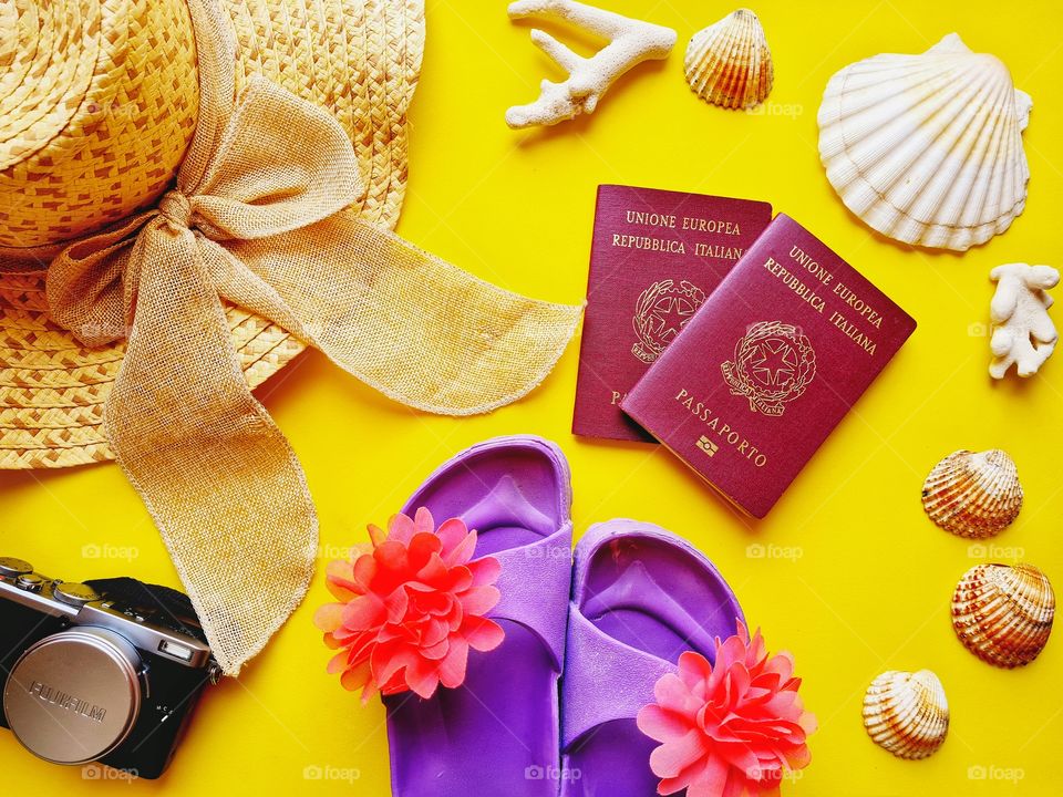flat lay with straw hat, passports, camera and colorful beach slippers on a yellow background (summer and travel concept)