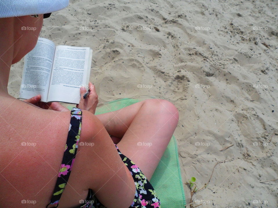 A girl in a sarafan sits on the sand and reads a book