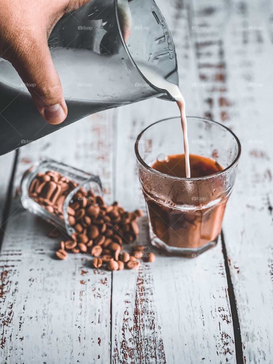 Pouring milk into a cup of coffee with spilled coffee beans on the side