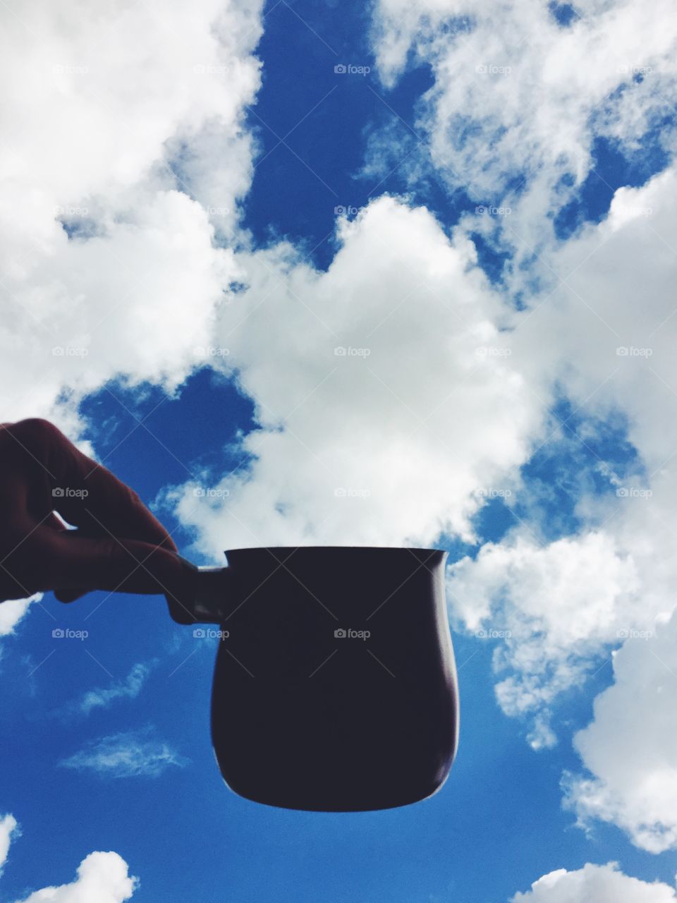 Hand holding mug against cloudy sky