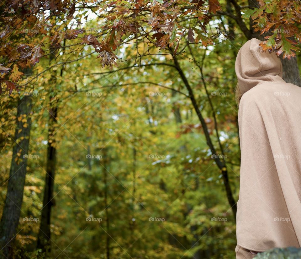 Fall-tale; Woman walking through an Autumn forest wearing a hooded cloak
