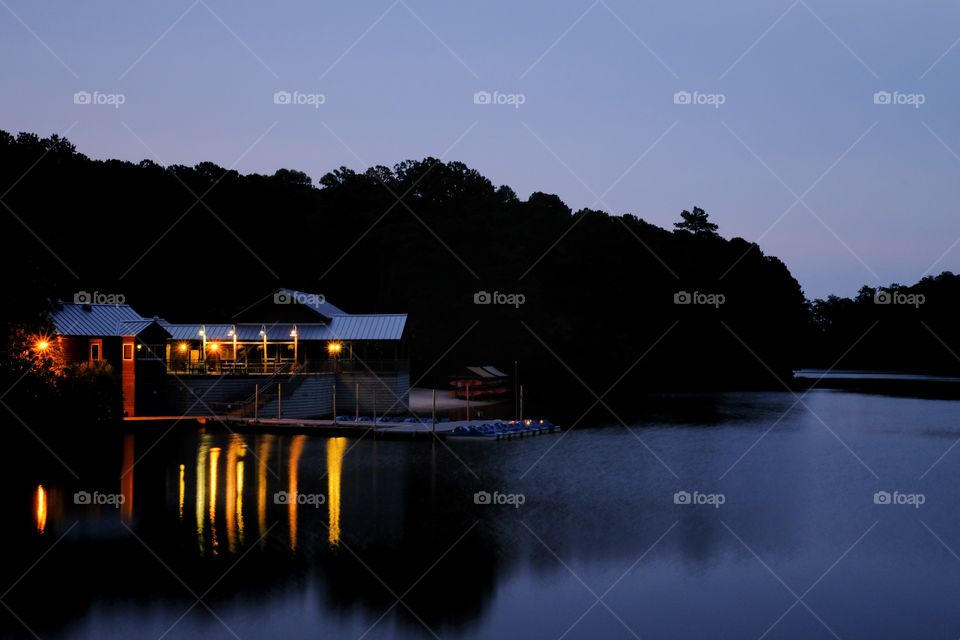 A beautifully lit boathouse casts vivid reflections on the water’s surface during the early morning twilight. Lake Johnson Park is a outdoor jewel in Raleigh North Carolina. 