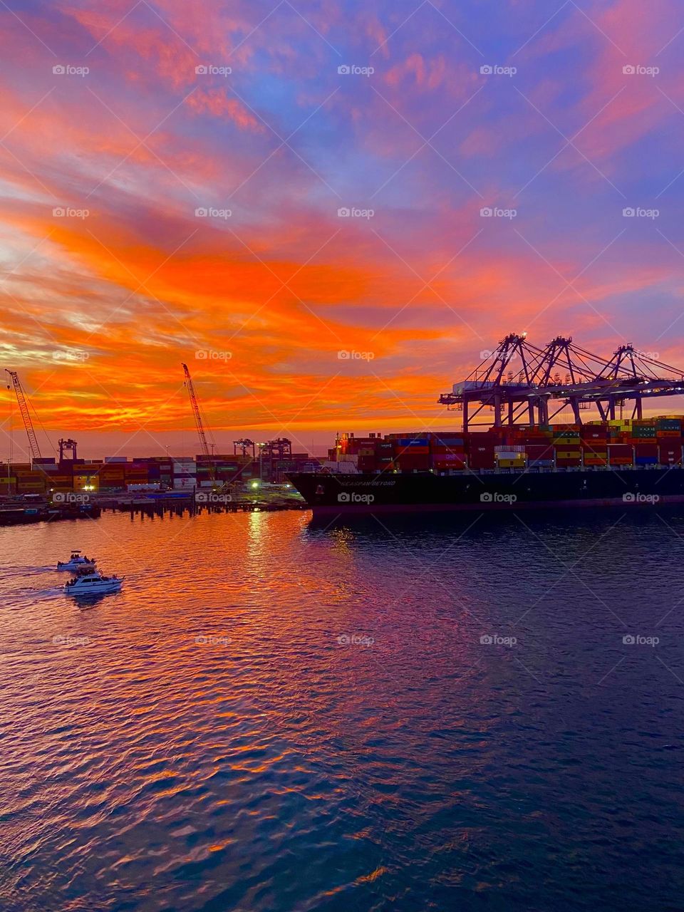 A cargo ship docked against a vibrant orange and blue sky and sea.
