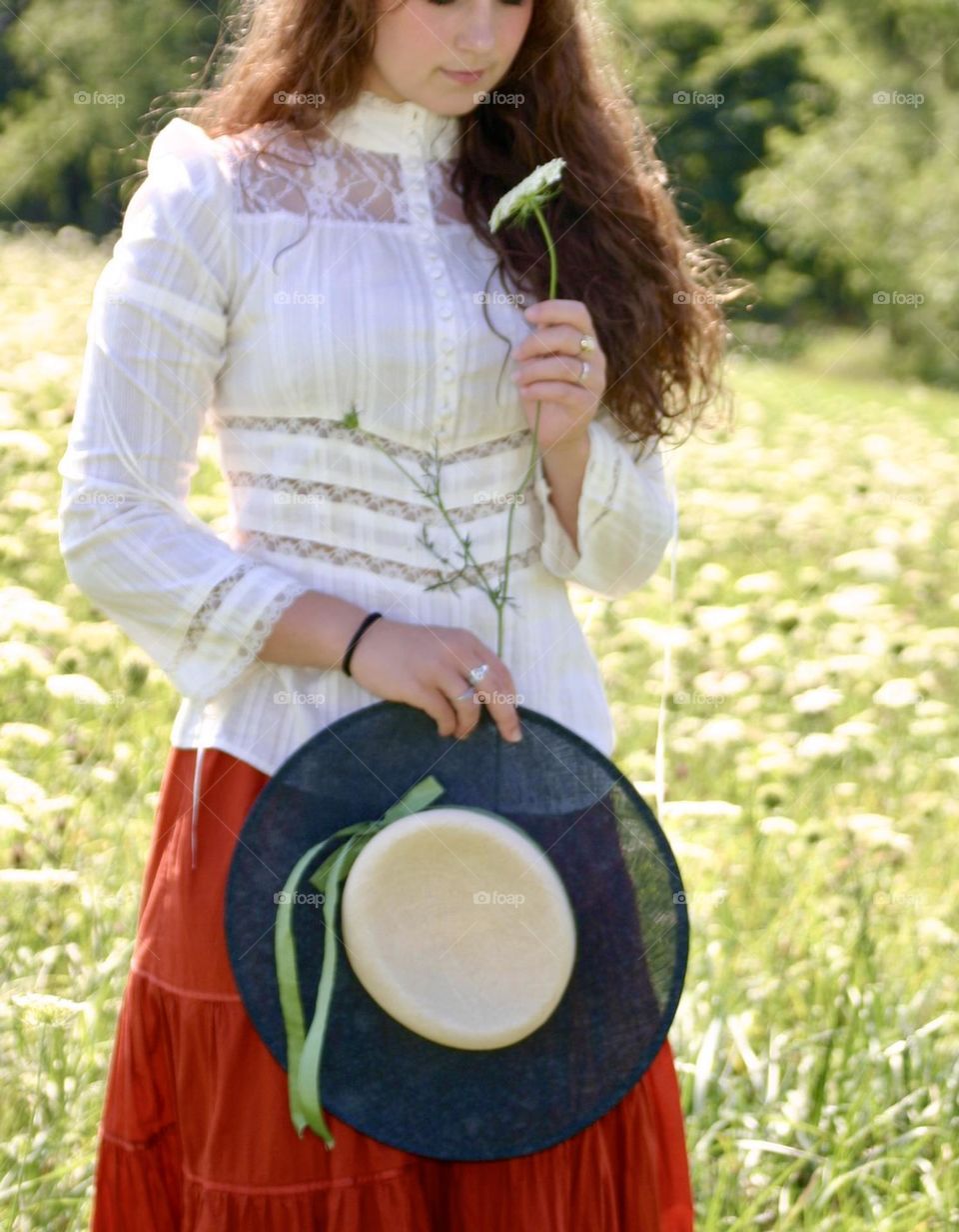 Girl in a field of white flowers holding a flower and a hat