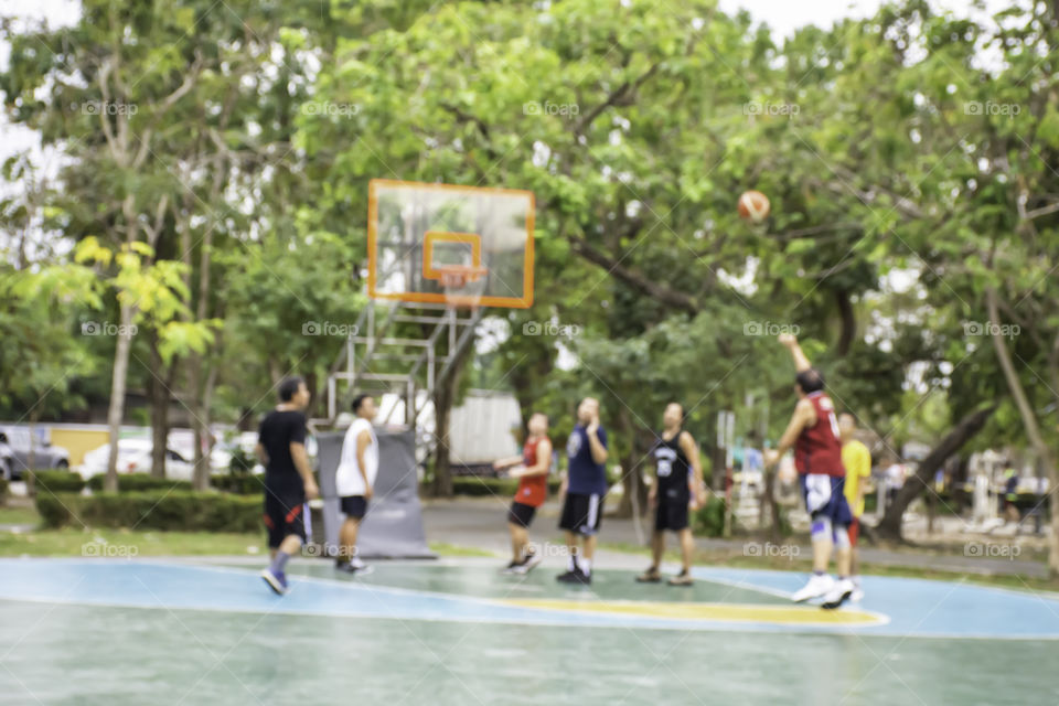 Blurry image of elderly men and teens playing basketball in the morning at BangYai Park , Nonthaburi in Thailand.