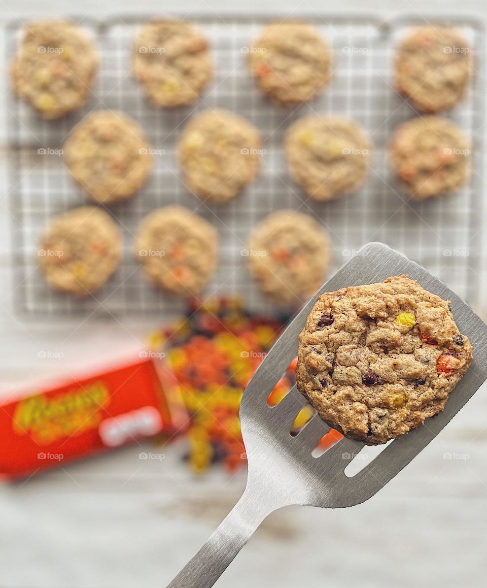 Placing cookie onto a cooling rack, cookie on a spatula with more freshly baked cookies in the background with Reese’s Pieces Candy, delicious homemade treats, mommy and toddler bake cookies together, mother makes cookies for toddler, enjoying cookie