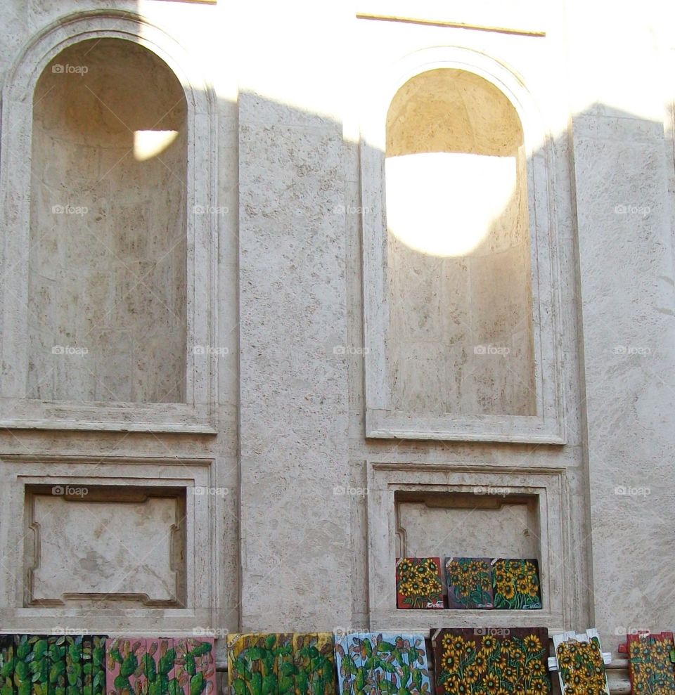 Italian street art of vibrant flowers lined along a white washed building with accented arched niches 