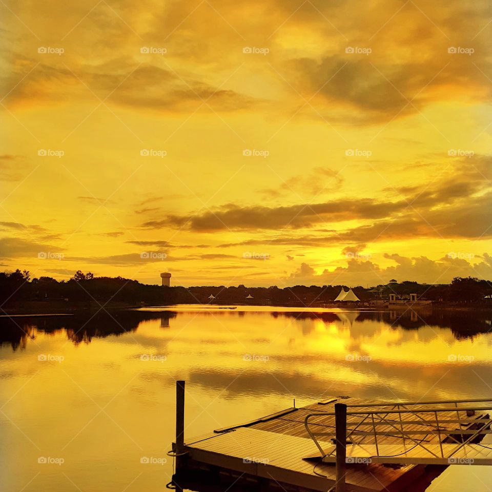 A golden yellow sunrise over the lake and dock at Cranes Roost Park in Altamonte Springs, Florida.