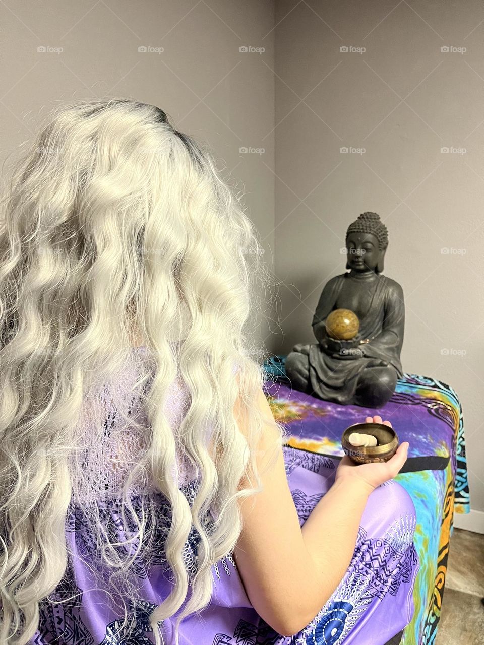 A woman meditating with a Buddha statue and a singing bowl in hand.