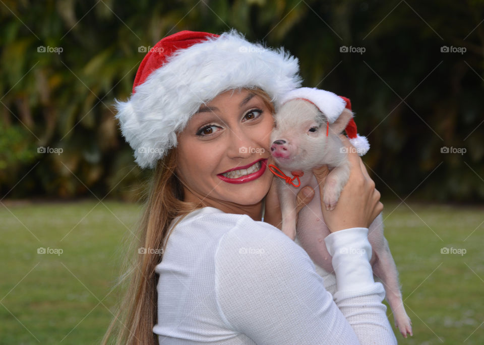 Woman and piglet wearing Santa's hat