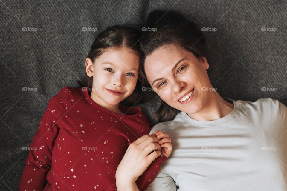 Close up portrait of happy Mom and daughter together lying on blanket at the home, view from top