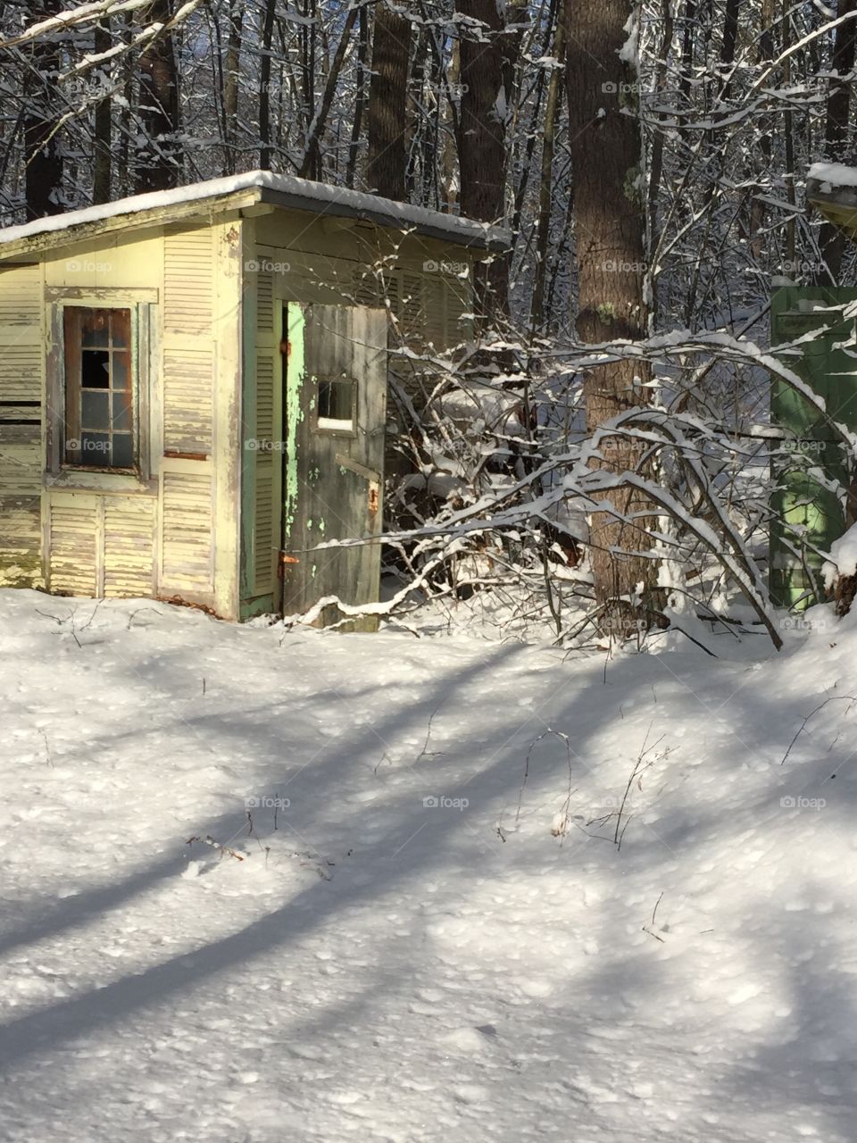 Winter in New England. Little yellow work shed being loved by the sunlight on a cold and snowy morning. 