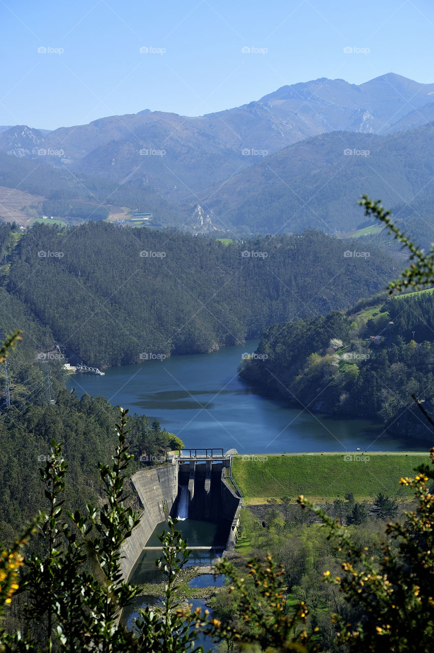 Dorias Reservoir with dam of hydroelectric power station in the middle of the forest and next to the mountains, Asturias (Spain).