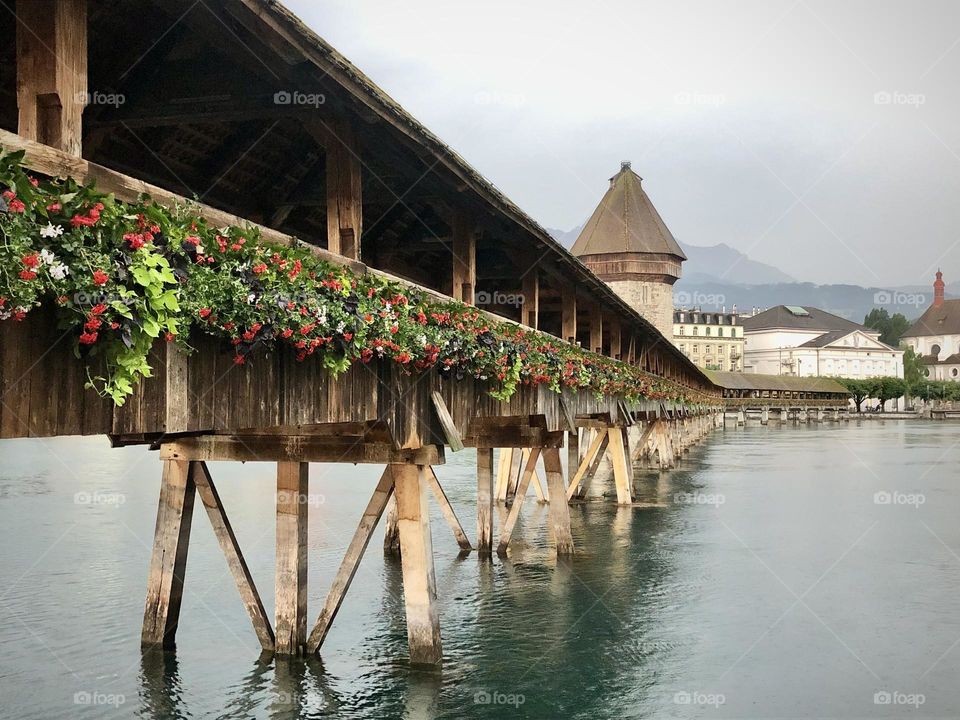 A romantic wooden covered bridge connects pedestrian sidewalks along the river in Lucerne, Switzerland 