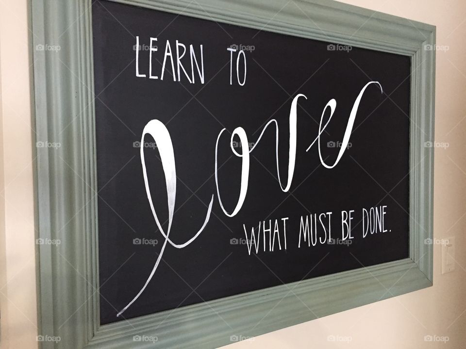 Learn To Love What Must Be Done. Written with white paint on a framed black board.