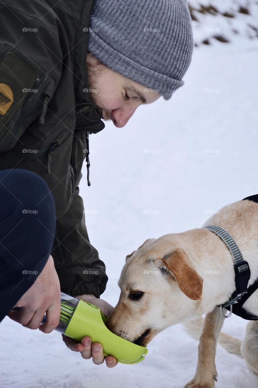 A man giving dog water on a walk in winter