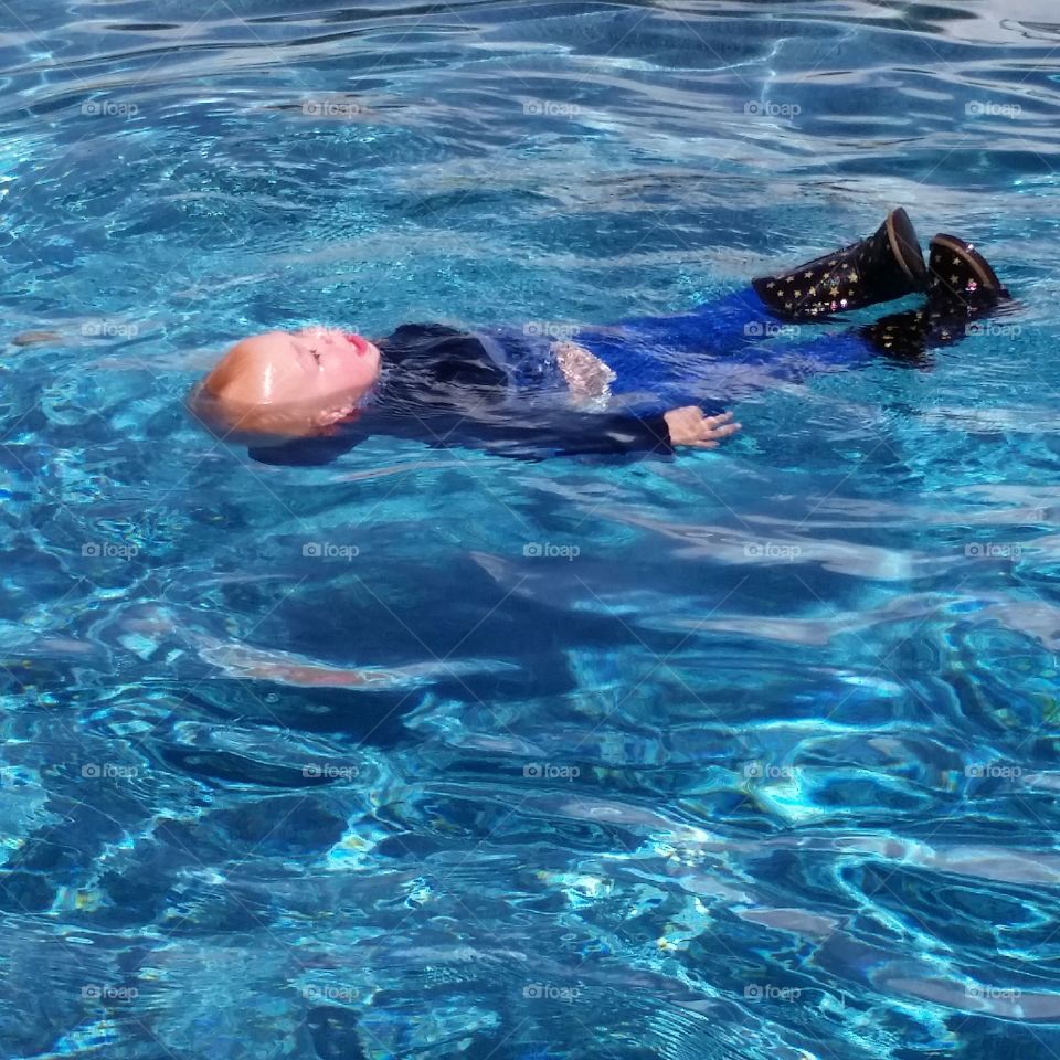 Baby floating in swim lesson. This baby is 18 months and has learned to swim and float to safety. He is swimming with winter clothes as a precaution.