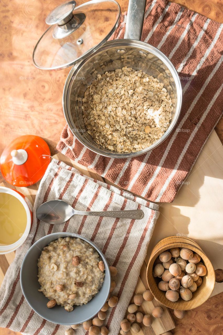Cooked oatmeal in a deep gray plate with hazelnuts and honey.