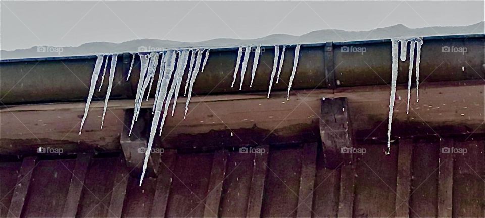 Icicles hang from the gutters beneath the snow covered roof of a house in “Kochel”, a resort town north of the “Alps” in “Bavaria”, Germany. It is known for the lake it is next to and natural hot springs, spas and saunas. 2024. Hypnotic Productions
