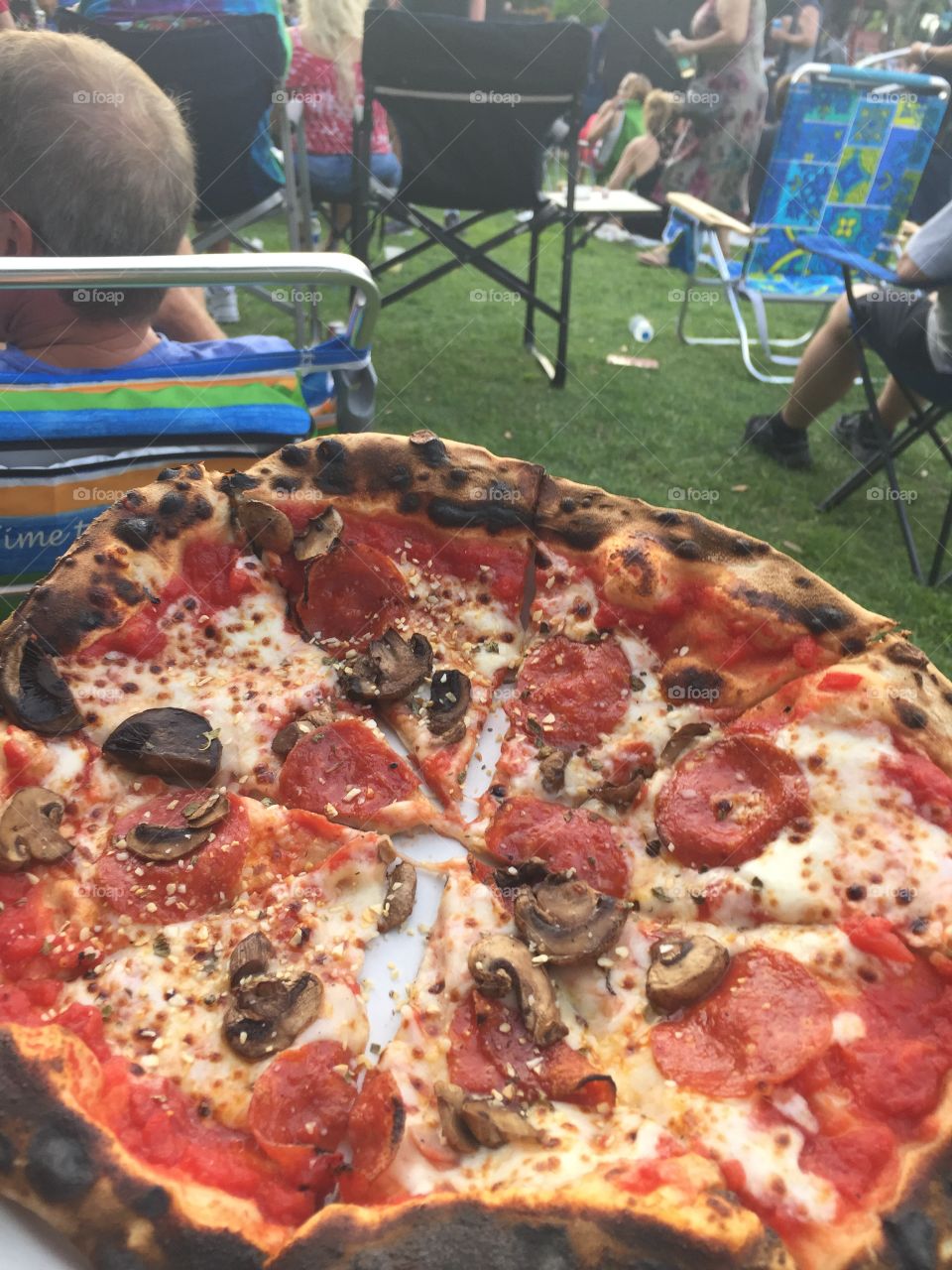 Holding a whole oven fired pizza with pepperoni and mushrooms at an outdoor concert