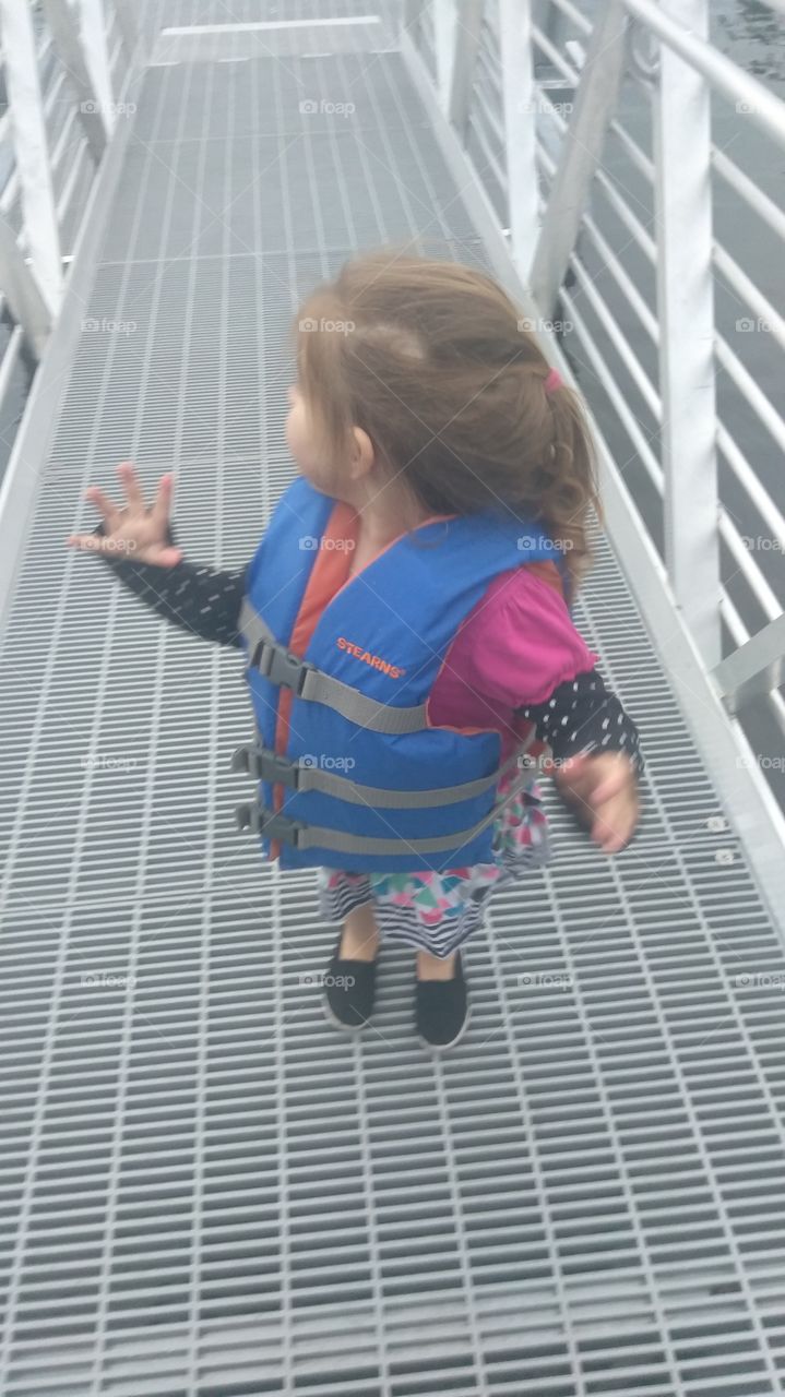 toddler wearing a life jacket k the ramp that leads down to the dock.