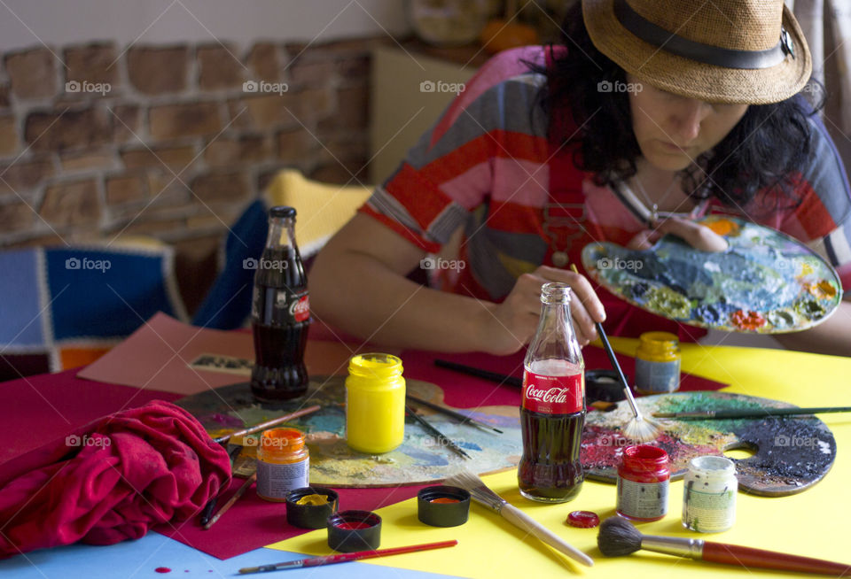 A woman painting on the table, colorful workplace, Coca-Cola bottles on the table