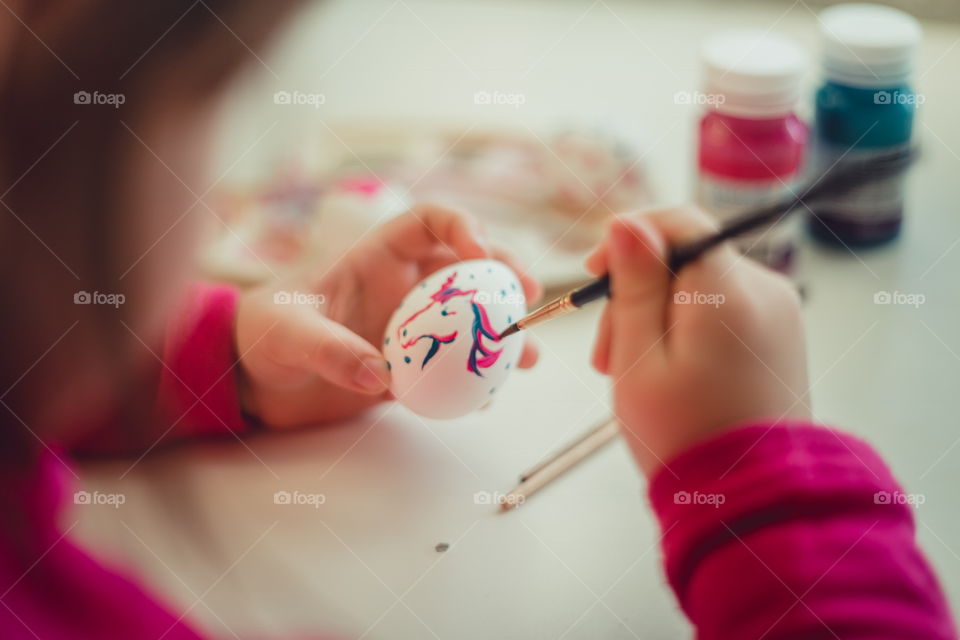 Little girl painting the Easter egg at home