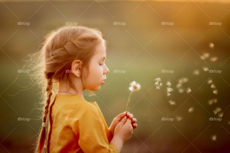 Little girl blowing dandelion at sunset