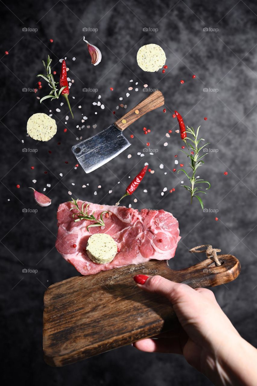 levitation from a cutting board, a piece of marbled meat with ingredients, spices, garlic, oil, hot red pepper, rosemary
