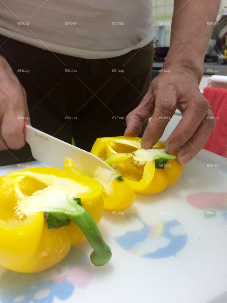 A woman is cooking and cutting yellow peppers on the cutting board. 
