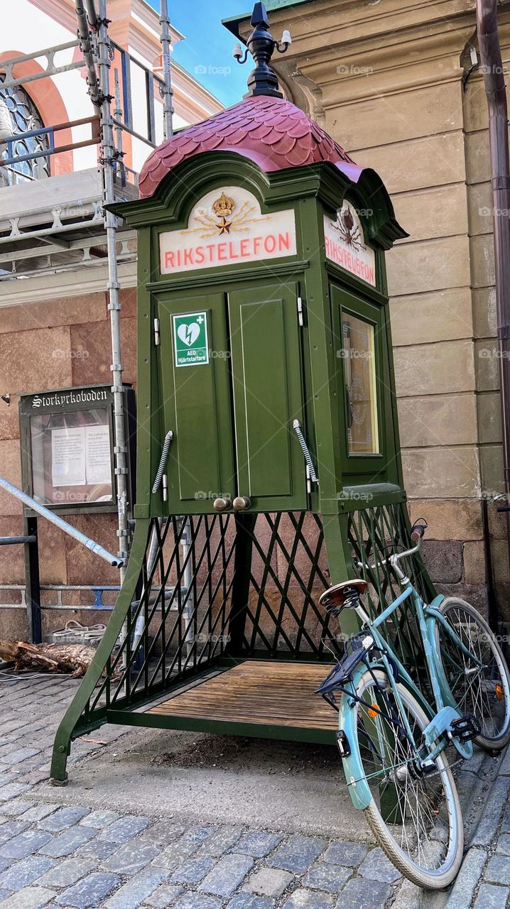 One lonely blue retro bicycle next to the old green phone booth with metal lattice 