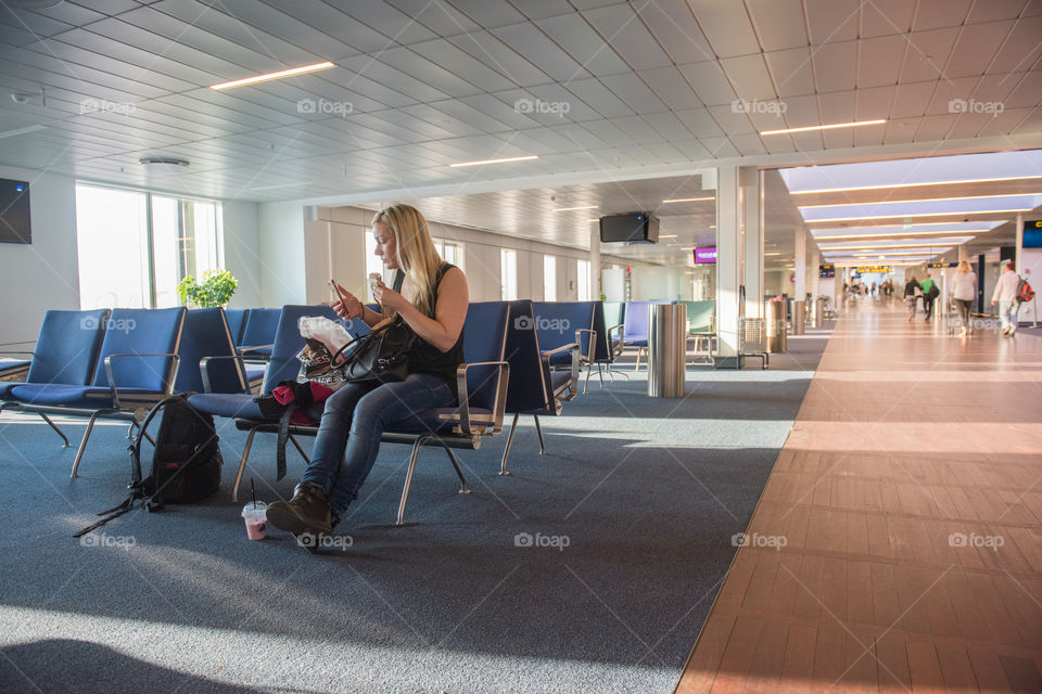 Woman waiting for her flight at Copenhagen airport in Denmark. She is eating and checking her social media on her phone.