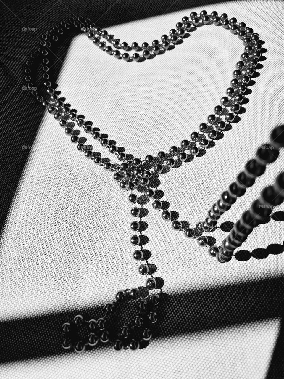 A pearl necklace laid as a heart with sunlight reflections through a window- shadow games